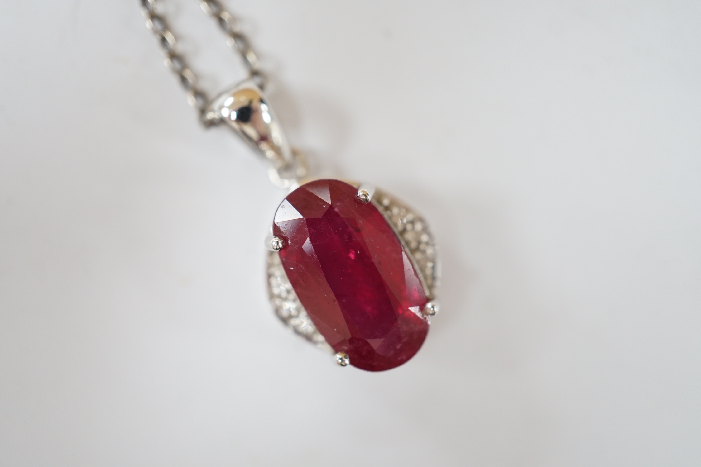 A modern 18ct white gold, ruby and diamond set oval cluster pendant, 24mm, on a white metal chain.